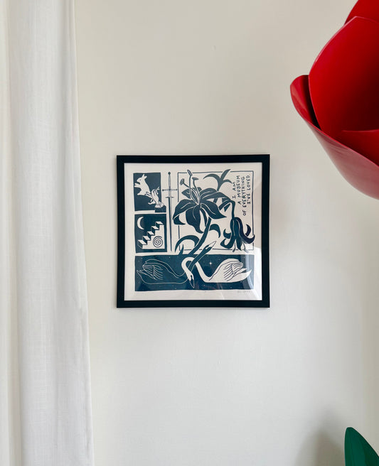 A framed screenprint featuring black and white imagery of swans and a lily on a wall.