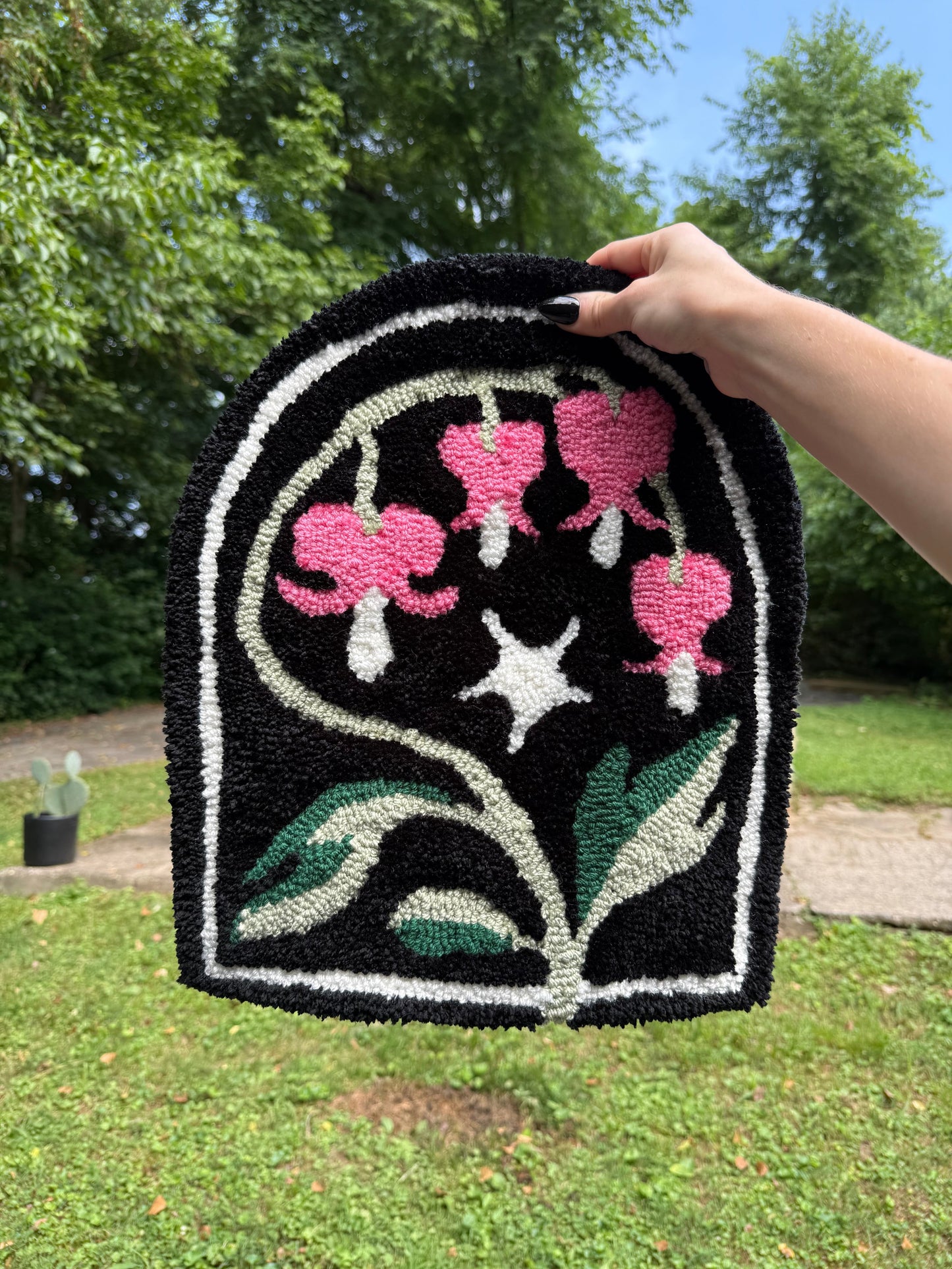 Hand holding a black floral-patterned rug with pink flowers and green leaves against a natural background.